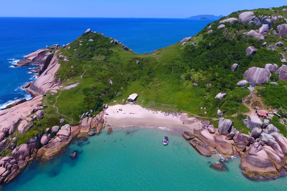 Vista aérea de praia isolada em Florianópolis, com areal claro entre morros verdes e mar turquesa