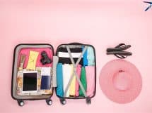 mala de viagem aberta com vários itens fundo rosa