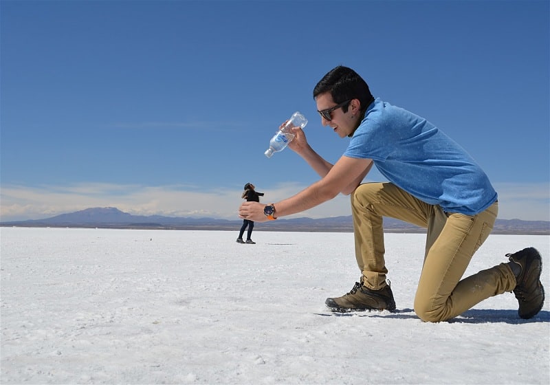 casal de turistas brincando com perspectiva na foto homem segurando garrafa de água