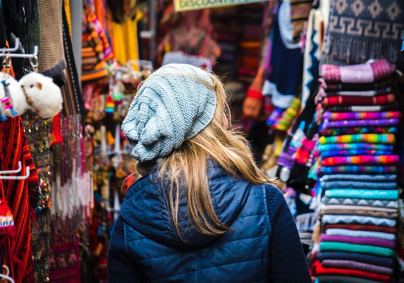 mulher loira com touca de costas andando por loja de artesanato peruano