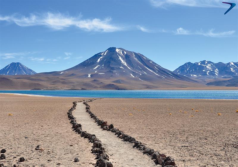 caminho de pedras em meio ao deserto com vulcão e montanhas ao fundo