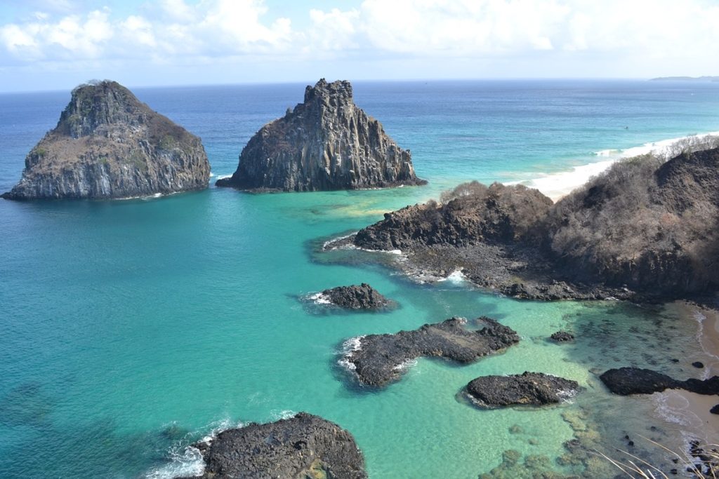 Vista panorâmica do Morro Dois Irmãos em Fernando de Noronha, com mar azul-turquesa, formações rochosas imponentes e paisagem paradisíaca.