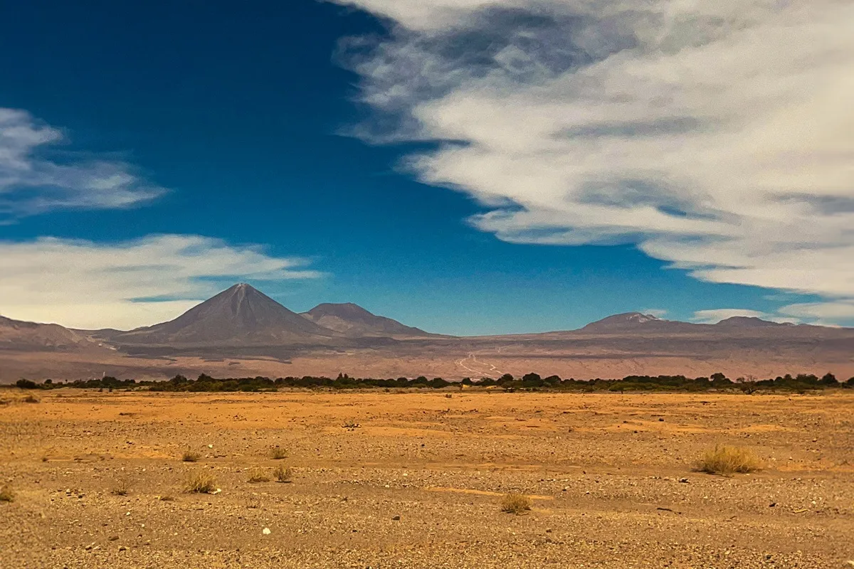 Vista panorâmica do Deserto do Atacama com montanhas ao fundo, céu azul intenso e nuvens espalhadas