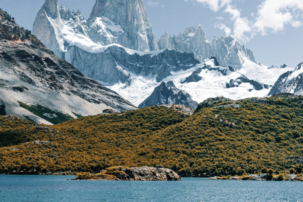 Vista panorâmica do Monte Fitz Roy coberto de neve, com colinas verdes e lago azul em primeiro plano, em El Chaltén, Patagônia Argentina