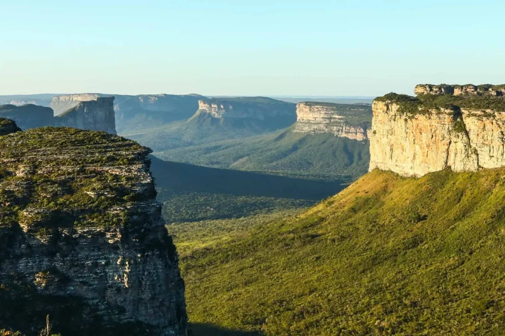 Formações rochosas da Chapada Diamantina com paredões de arenito, vales verdes e relevo montanhoso sob céu claro.