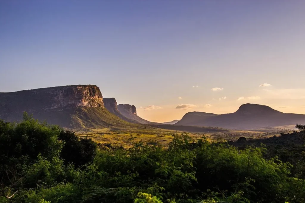 Vista do entardecer na Chapada Diamantina com montanhas, vales verdes e céu azul-alaranjado ao fundo.