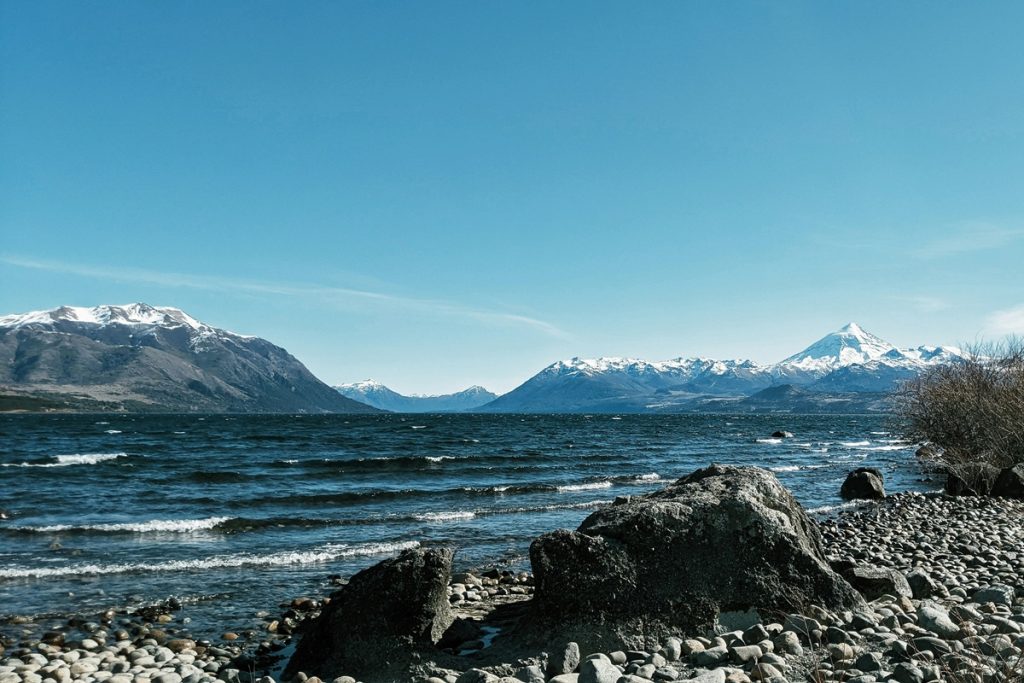 Vista panorâmica do lago em San Martín de Los Andes com pedras na margem e o vulcão Lanín coberto de neve ao fundo