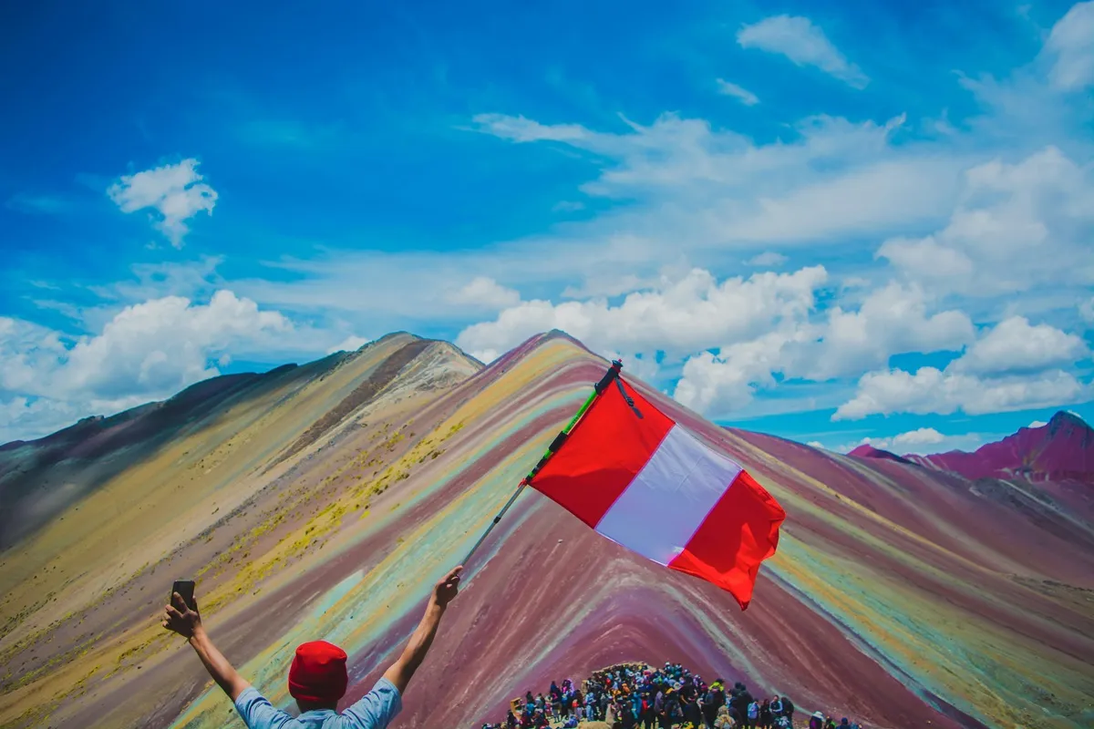Turista segurando a bandeira do Peru no topo da Montanha Colorida de Vinicunca, também conhecida como Montanha Arco-Íris.