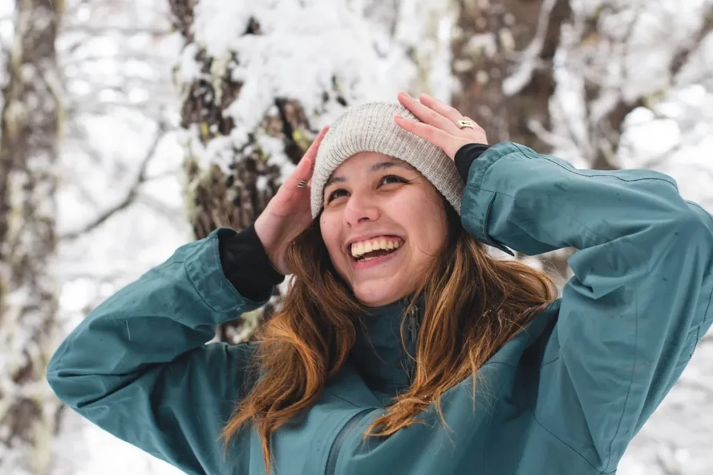 Mulher sorrindo na neve com casaco azul e touca de lã durante o inverno