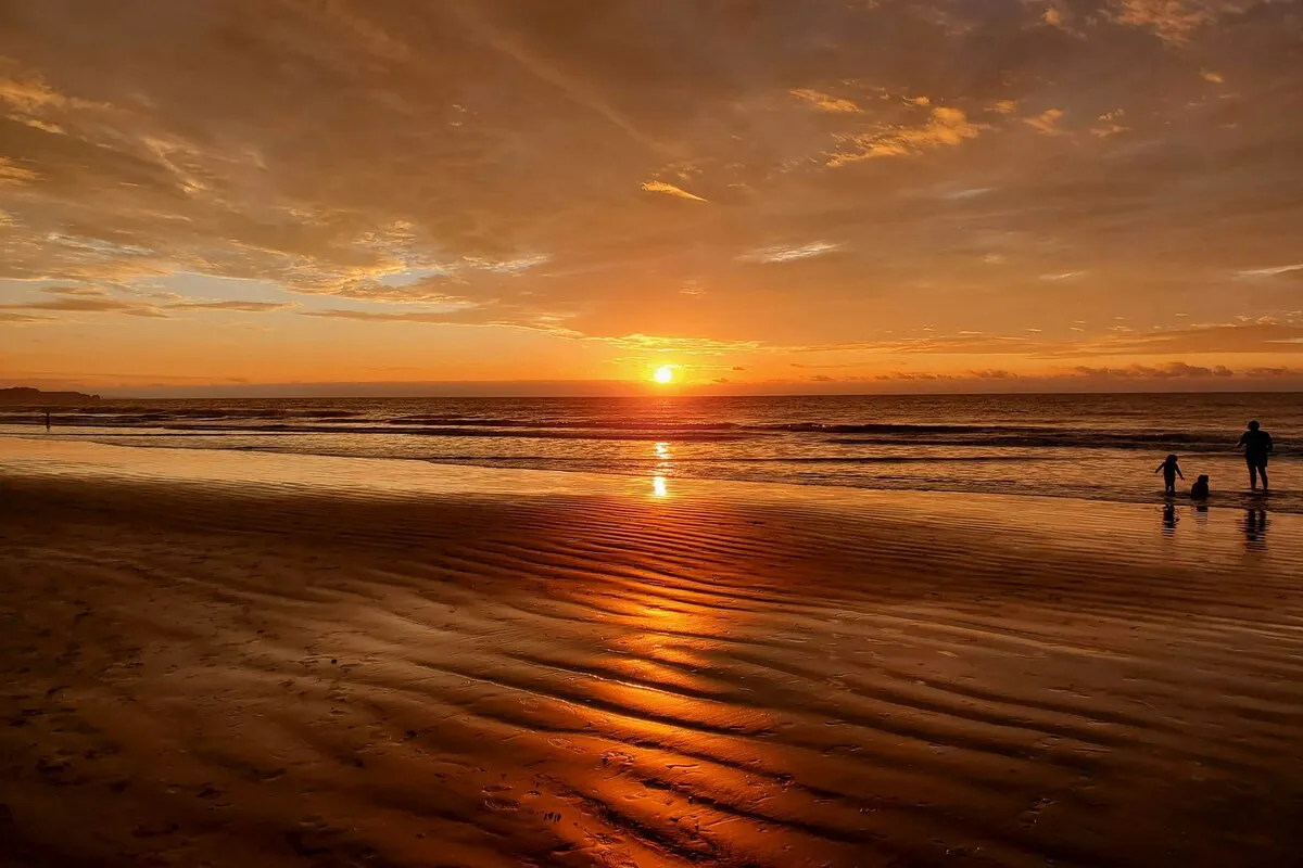 Pôr do sol dourado em praia equatoriana com silhuetas de pessoas brincando à beira-mar.