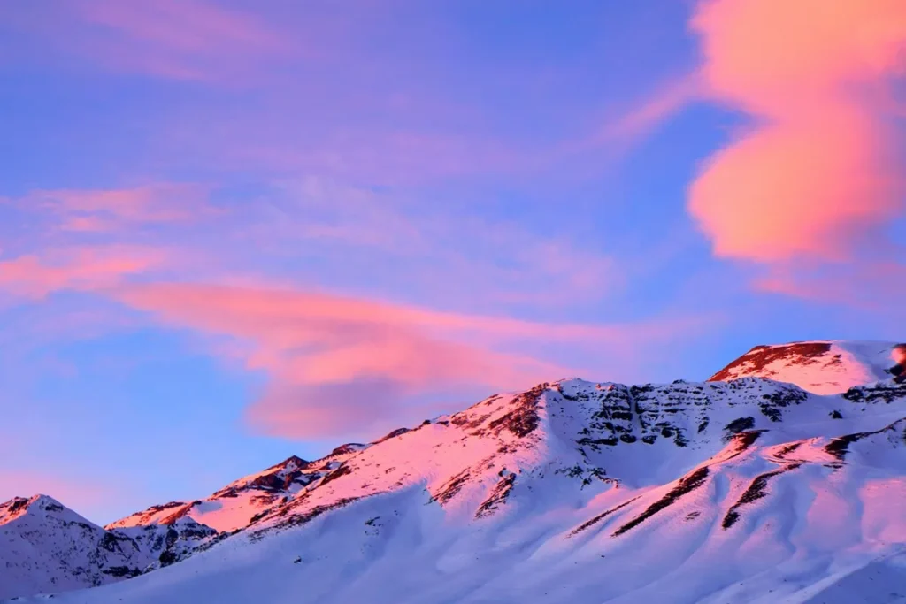 Montanhas nevadas de Farellones sob um céu ao amanhecer com nuvens cor-de-rosa e azul