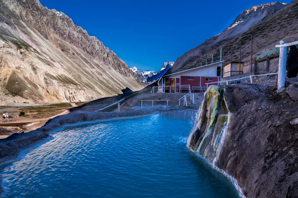 Bate volta nas Termas del Plomo, Chile, com piscina natural de águas termais azul-turquesa, montanhas e edifício rústico.