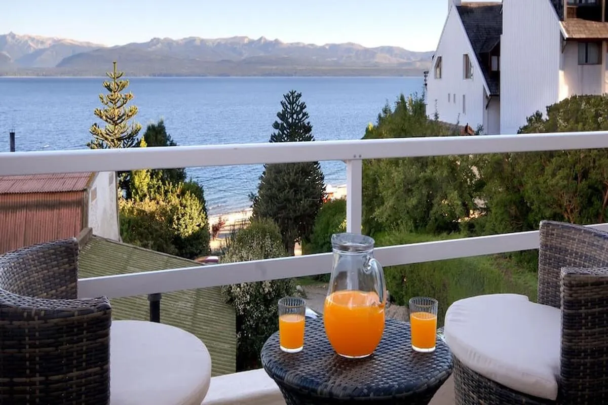 Varanda de quarto do melhor hotel em Bariloche com jarra de suco de laranja e vista para o lago e a praia