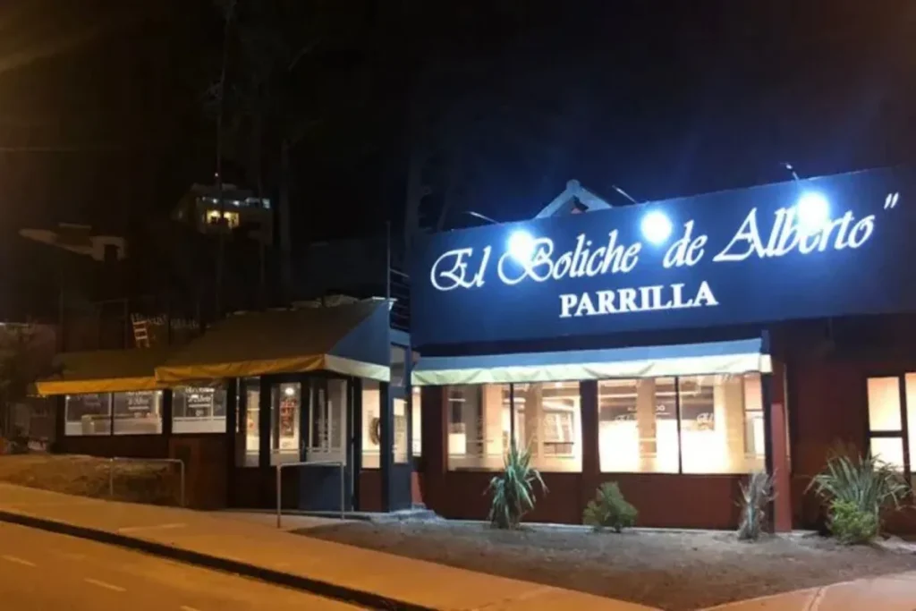 Fachada iluminada à noite do restaurante El Boliche de Alberto Parrilla em Bariloche, com janelas e letreiro do estabelecimento.