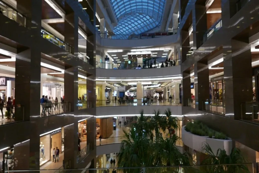 Vista interna e panorâmica do shopping Costanera Center, mostrando vários andares de lojas, pilares de sustentação e um teto de vidro que permite a entrada de luz natural.