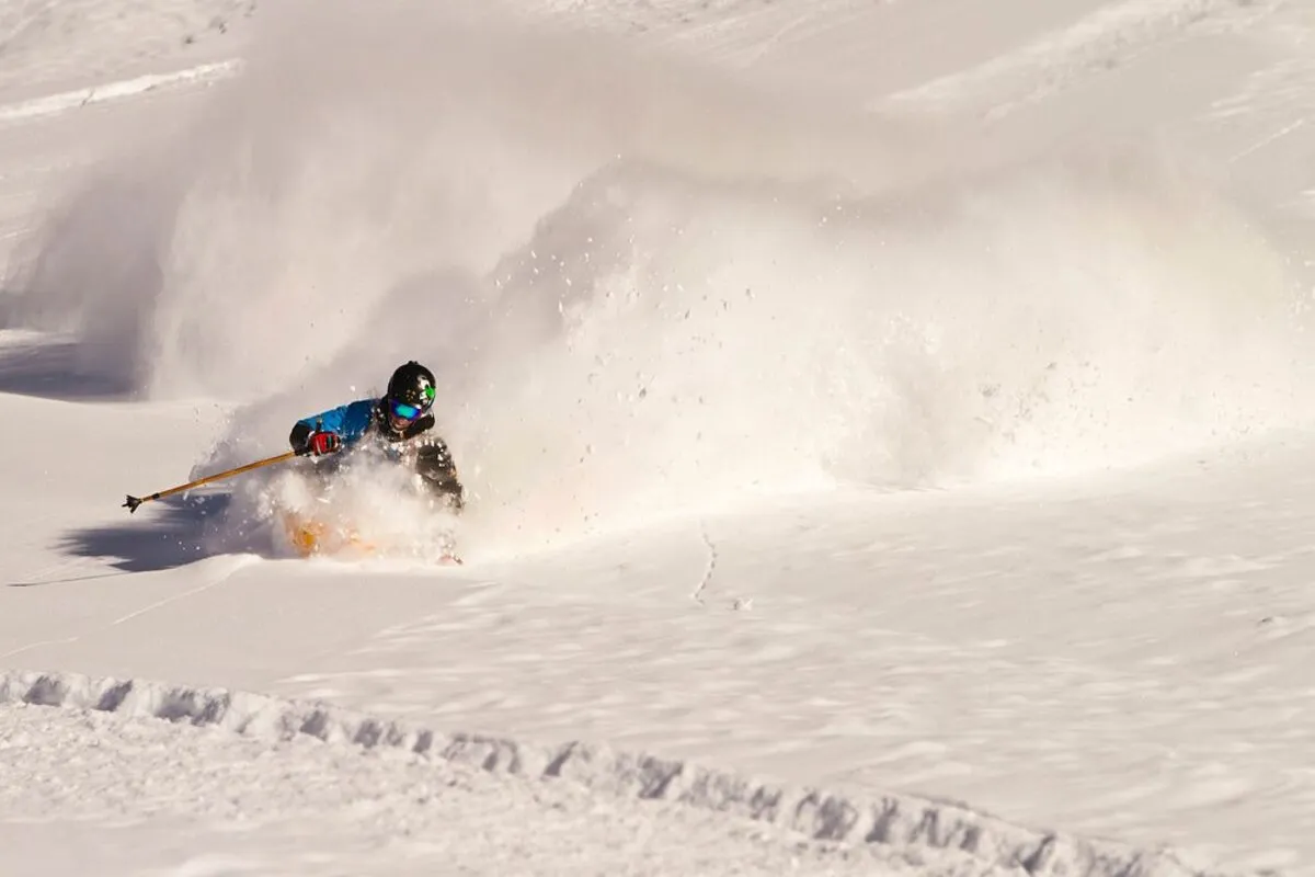 Esquiador em movimento, levantando uma grande nuvem de neve em pó enquanto faz uma curva fechada nas pistas de El Colorado.