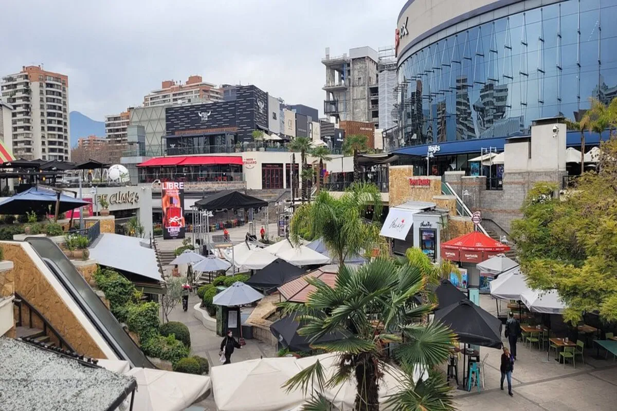 Vista aérea de um shopping a céu aberto com restaurantes, quiosques, espreguiçadeiras com guarda-sóis e edifícios modernos ao fundo.