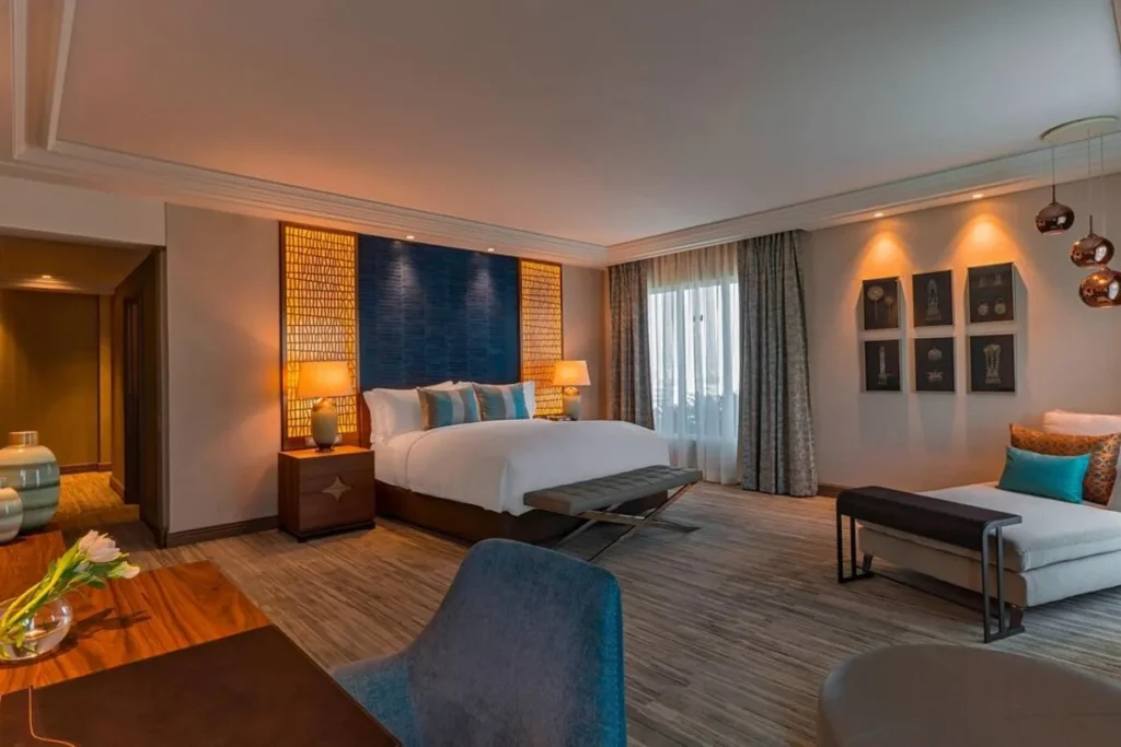 Quarto de luxo do The Ritz Carlton com cama grande, área de estar, iluminação quente e decoração elegante.
