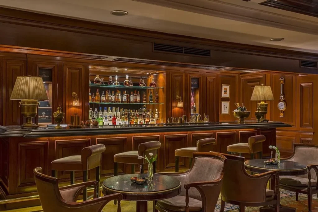 Interior de um bar de luxo, com balcão de madeira, banquetas estofadas e uma vasta seleção de bebidas, comum no The Ritz Carlton.