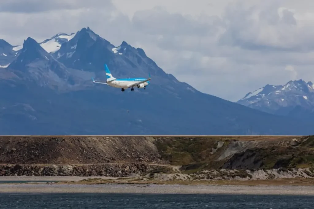 Avião da Aerolíneas Argentinas sobrevoando a pista do aeroporto de Ushuaia, com as montanhas da Cordilheira dos Andes ao fundo.