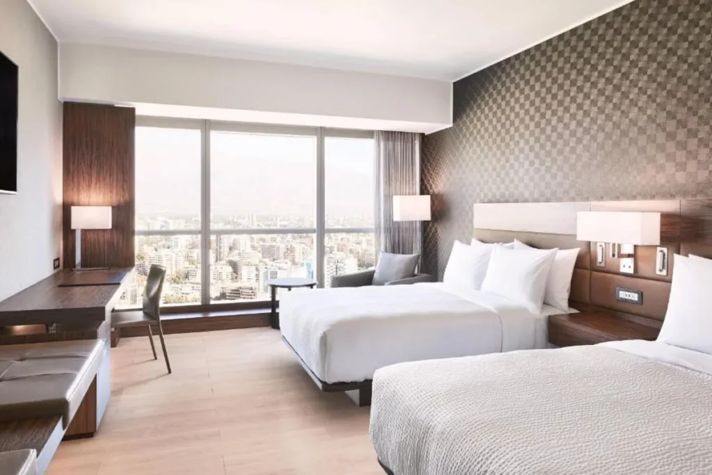Quarto moderno de um dos hotéis em Santiago, com duas camas de casal e uma grande janela com vista para a cidade.