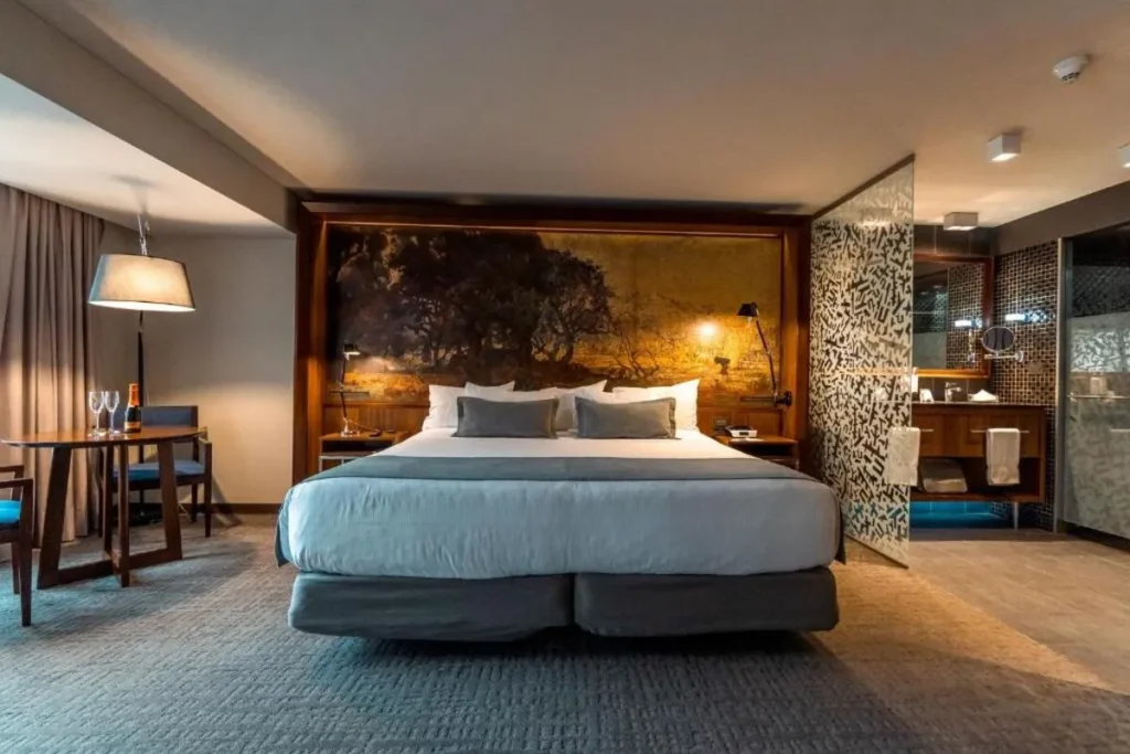 Interior de um quarto de luxo, com cama grande, área de estar e banheiro integrado, típico dos hotéis em Santiago.