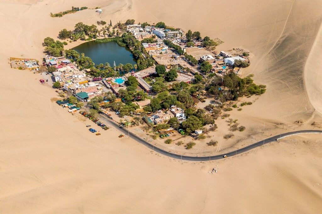 Vista aérea completa do Oásis de Huacachina rodeado por dunas de areia no deserto do Peru.
