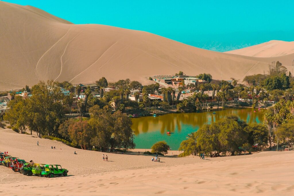 Vista panorâmica do Oásis de Huacachina cercado por dunas gigantes no deserto peruano.