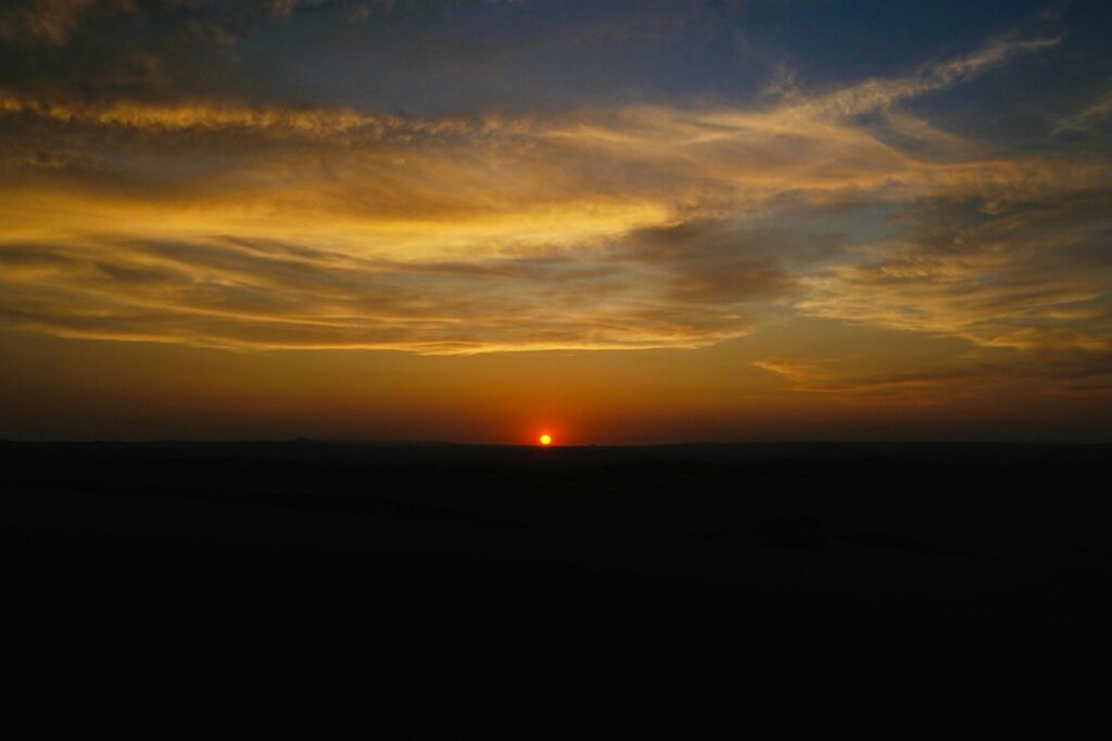 Pôr do sol nas dunas de Huacachina com céu alaranjado e horizonte desértico no Peru.