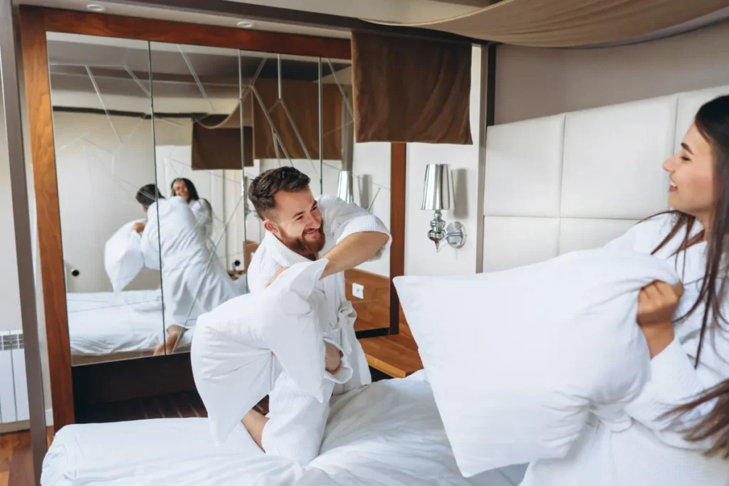 Casal de roupão branco em cama de hotel durante uma estadia noturna.