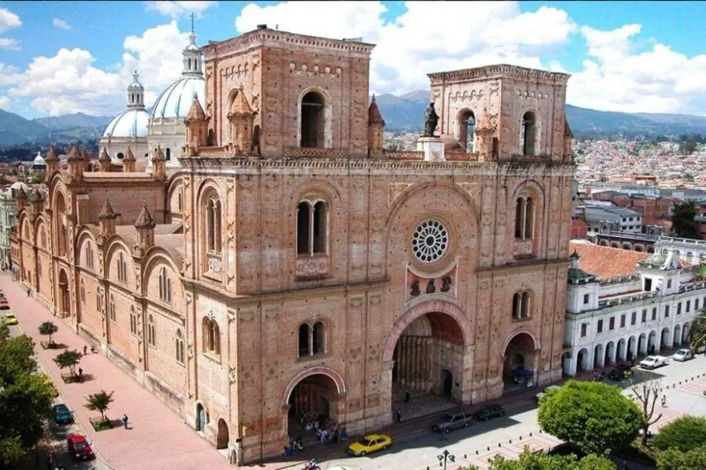 A Catedral da Imaculada Conceição em Cuenca, Equador, com suas torres e cúpulas de tijolos avermelhados sob um céu azul.