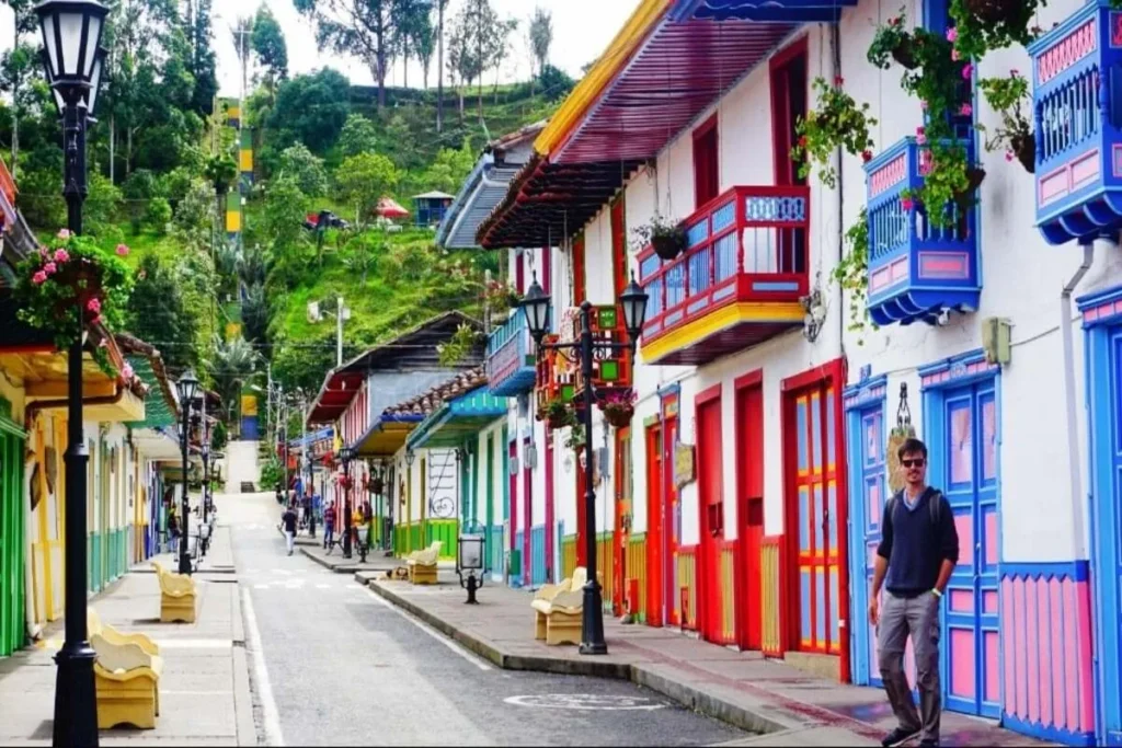 Homem caminhando na calçada de uma rua com casas coloridas e varandas decoradas em Salento, Colômbia.