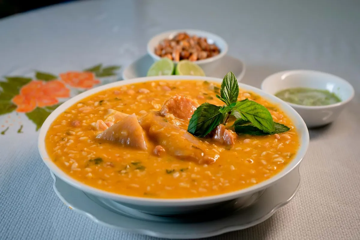 Um prato de sopa ou guisado peruano servido em uma tigela branca, com pedaços de carne e um galho de hortelã, em um restaurante em Trujillo, Peru.