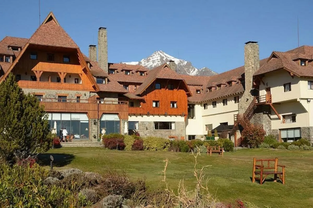 Fachada do Hotel Llao Llao em Bariloche, com sua arquitetura em estilo alpino, cercada por jardins, com uma montanha nevada ao fundo.