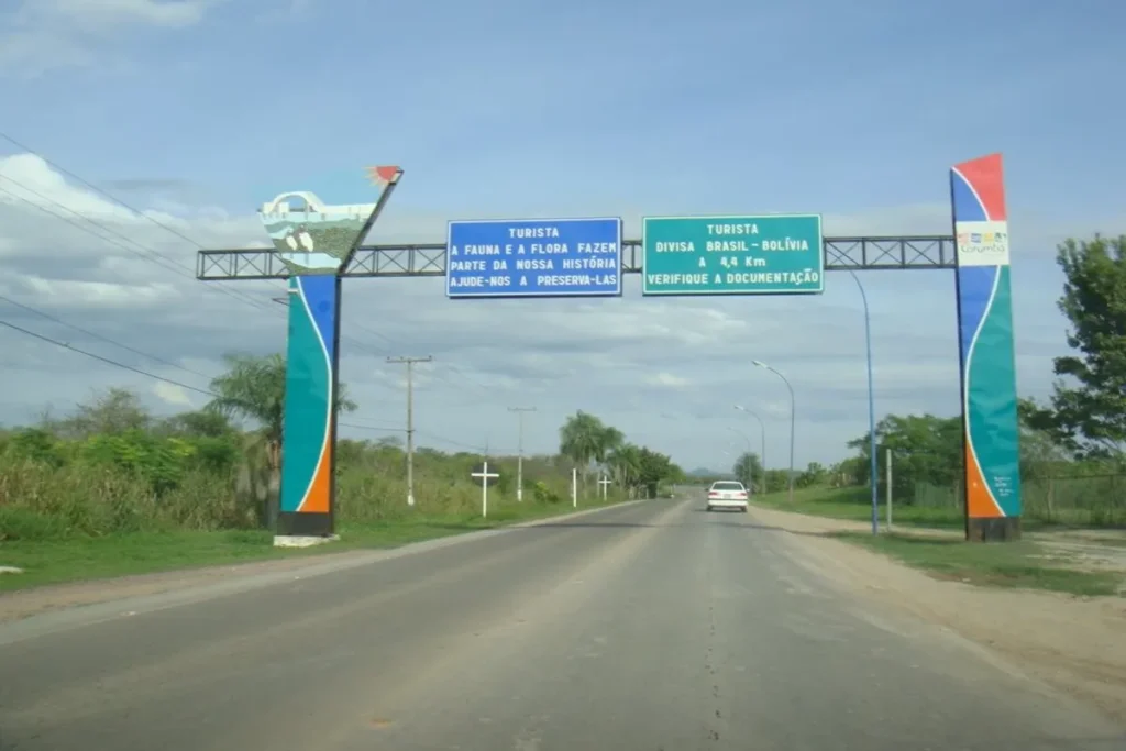 Estrada de fronteira Bolívia Brasil com um arco colorido e placas de sinalização, mostrando a divisa a 4,4 km.
