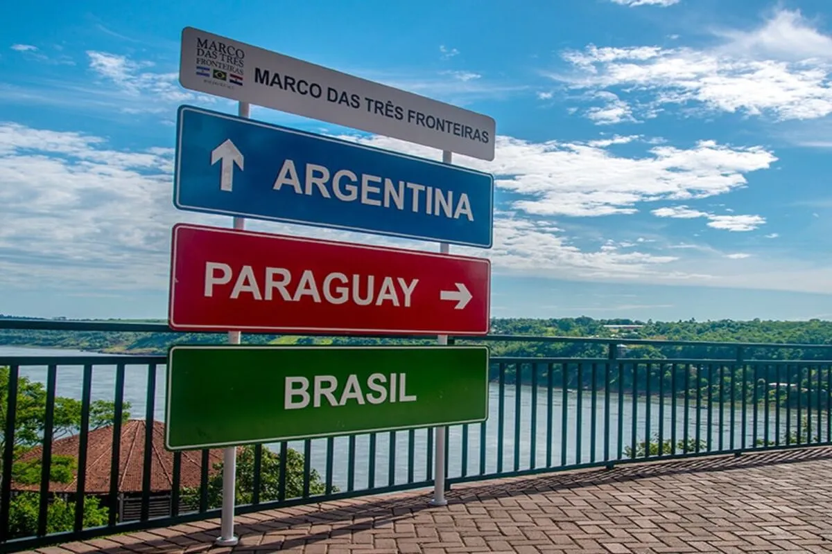 Placa turística do Marco das Três Fronteiras em Puerto Iguazú, Argentina, indicando os caminhos para Argentina, Paraguai e Brasil com vista panorâmica do Rio Iguaçu.