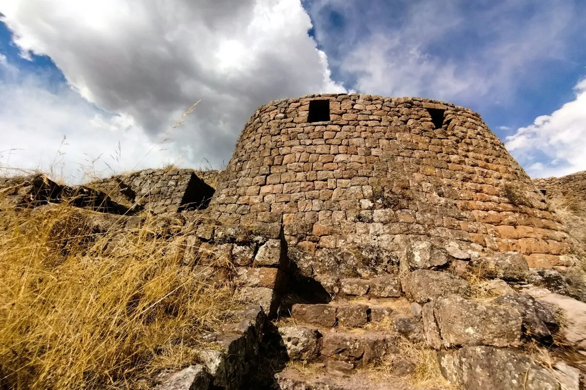 Estrutura circular e fortificada de pedra inca nas ruínas de Pisac, com escadas e montanhas ao fundo, Vale Sagrado do Peru.