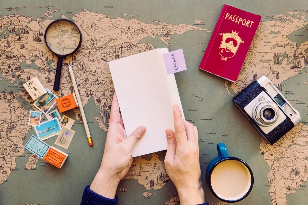 Vista de cima de mãos manuseando um caderno e planejando rota de viagem em um mapa, com passaporte, câmera e lupa ao redor, checando os documentos para entrada no Chile.