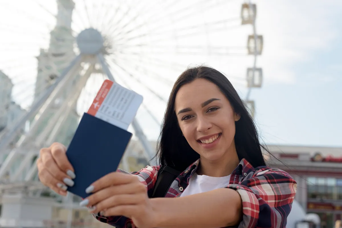 Mulher jovem sorridente mostrando passaporte com passagem aérea e seguro viagem internacional em mãos antes de viagem internacional