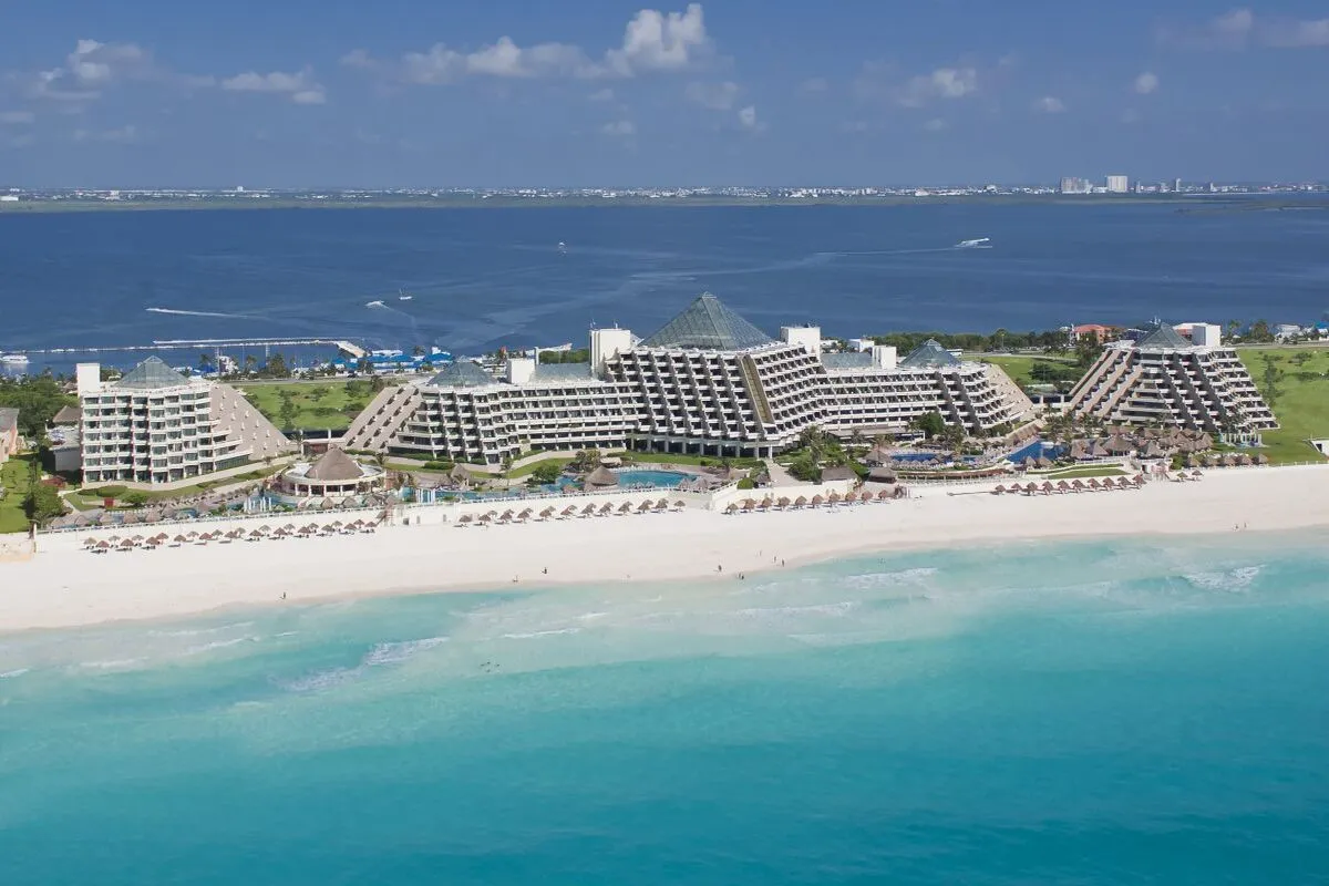 Resort all inclusive de arquitetura piramidal em Cancún ou no Caribe, com praia de areia branca e mar azul-turquesa sob sol forte.