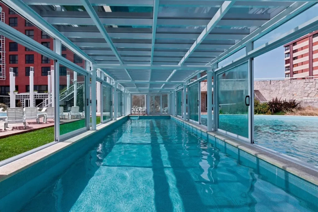 Piscina coberta e aquecida do hotel Sheraton Mar del Plata, com estrutura de vidro e vista para a área externa ensolarada.