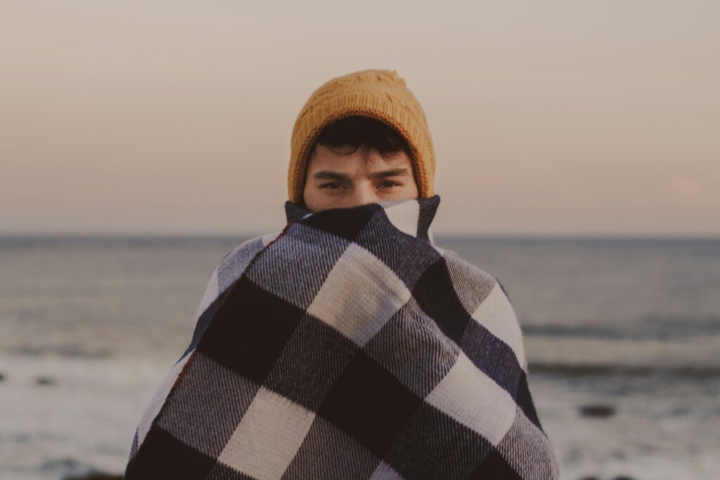Pessoa usando touca e cobertor xadrez em frente ao mar durante um dia frio no Uruguai.
