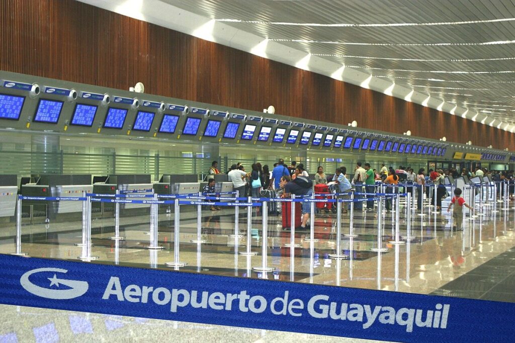 Área de check-in do Aeroporto Internacional de Guayaquil com passageiros, balcões de atendimento e painéis de voos.