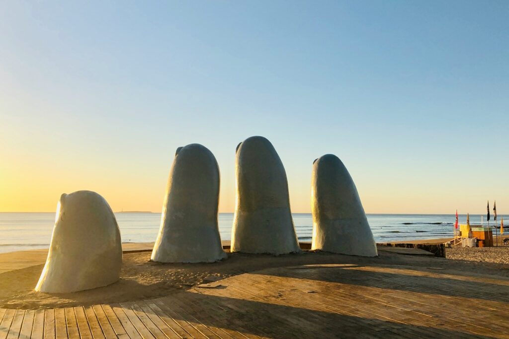 Escultura La mano em Punta del Este, no Uruguai, com praia e mar ao fundo durante o pôr do sol.