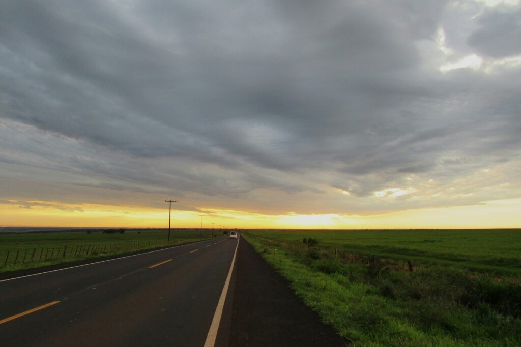 Estrada rural no Paraguai atravessando campos verdes sob céu nublado durante o pôr do sol.