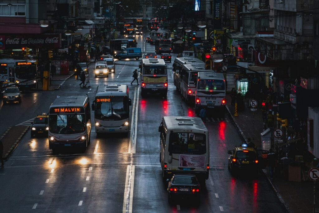 Avenida movimentada em Montevidéu com ônibus, carros, pedestres e pista molhada após chuva.