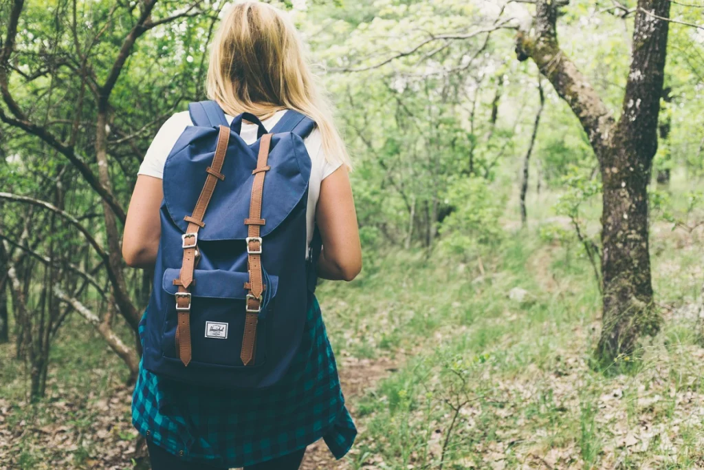 Mulher andando em floresta, com mochila nas costas.