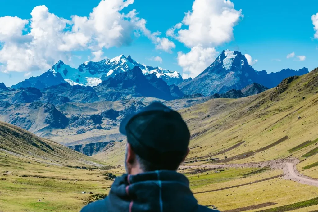 Homem observando cordilheira dos Andes com picos nevados sob céu azul, durante viagem pela América do Sul.