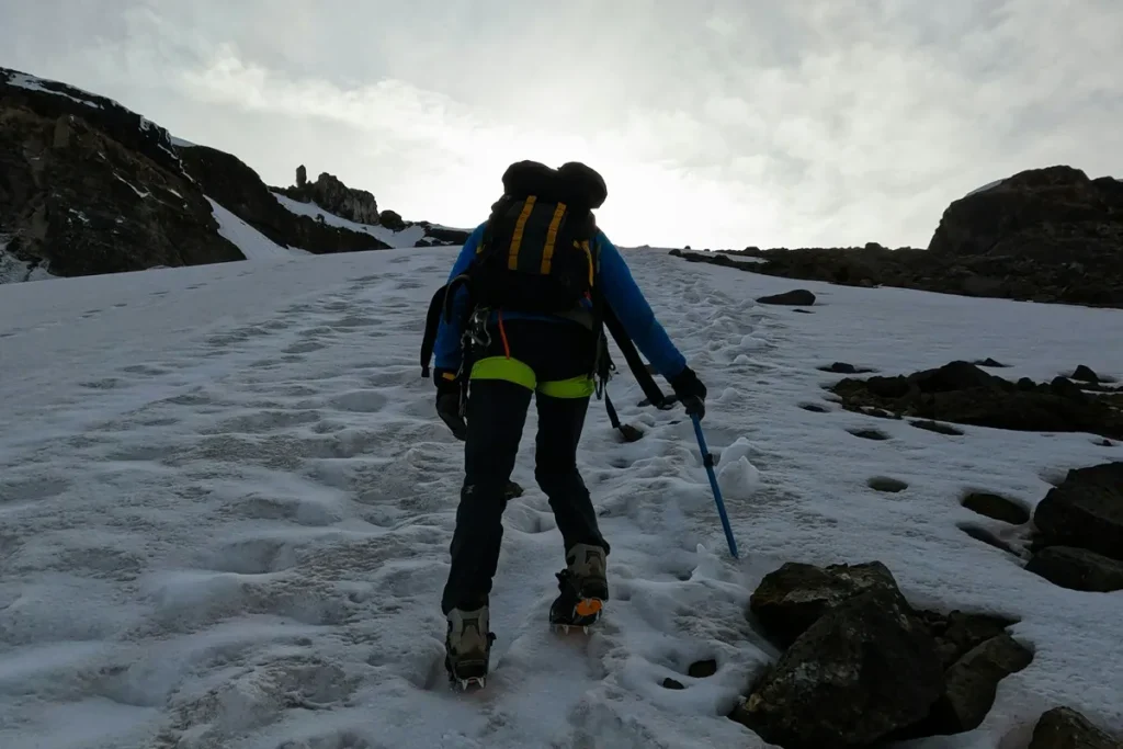 Por que escolher a Livare Viagens para sua viagem pela América do Sul? Montanhista com mochila e equipamento de gelo caminhando por uma encosta nevada rumo ao cume