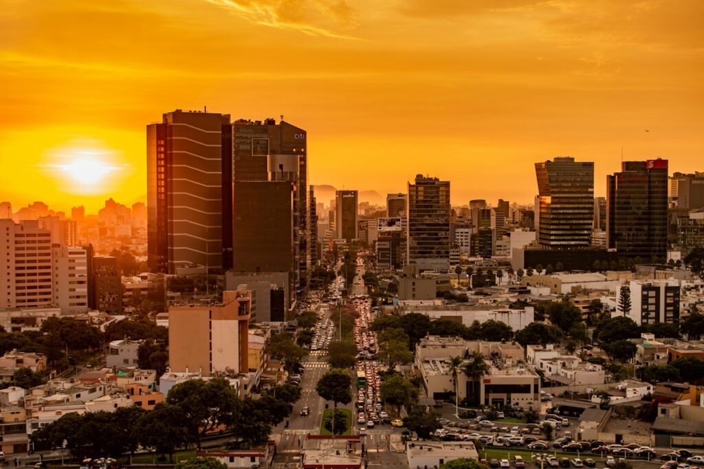 Vista aérea de Lima ao entardecer mostrando arranha-céus, avenida movimentada e o horizonte urbano da capital do Peru.